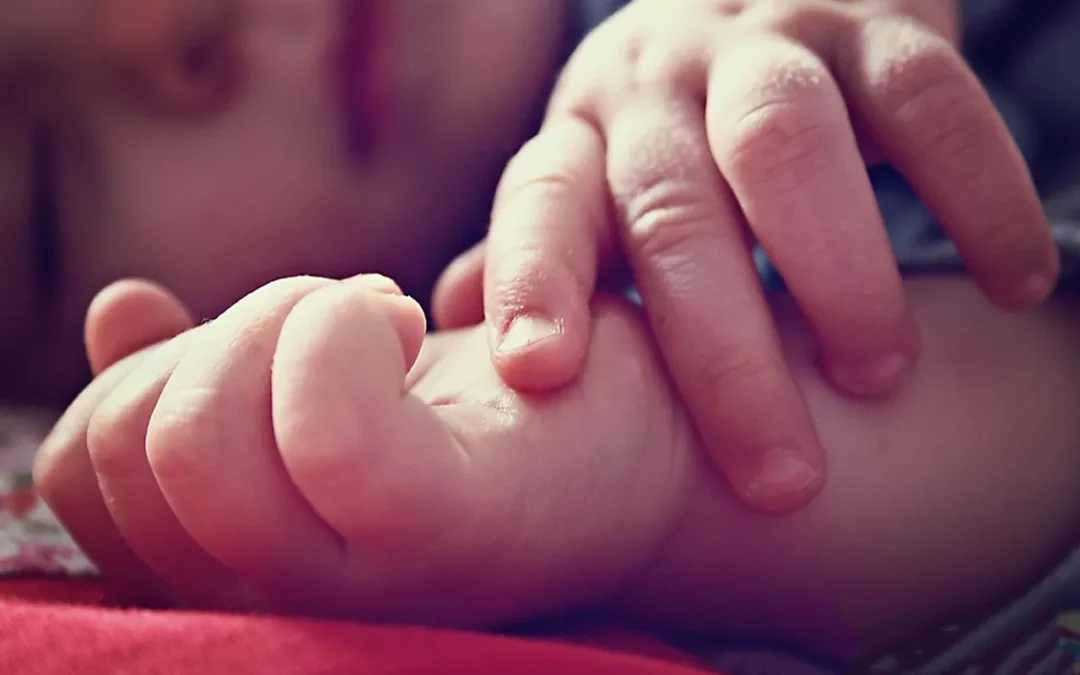 Bébé dormant, main posée sur une couverture rouge.