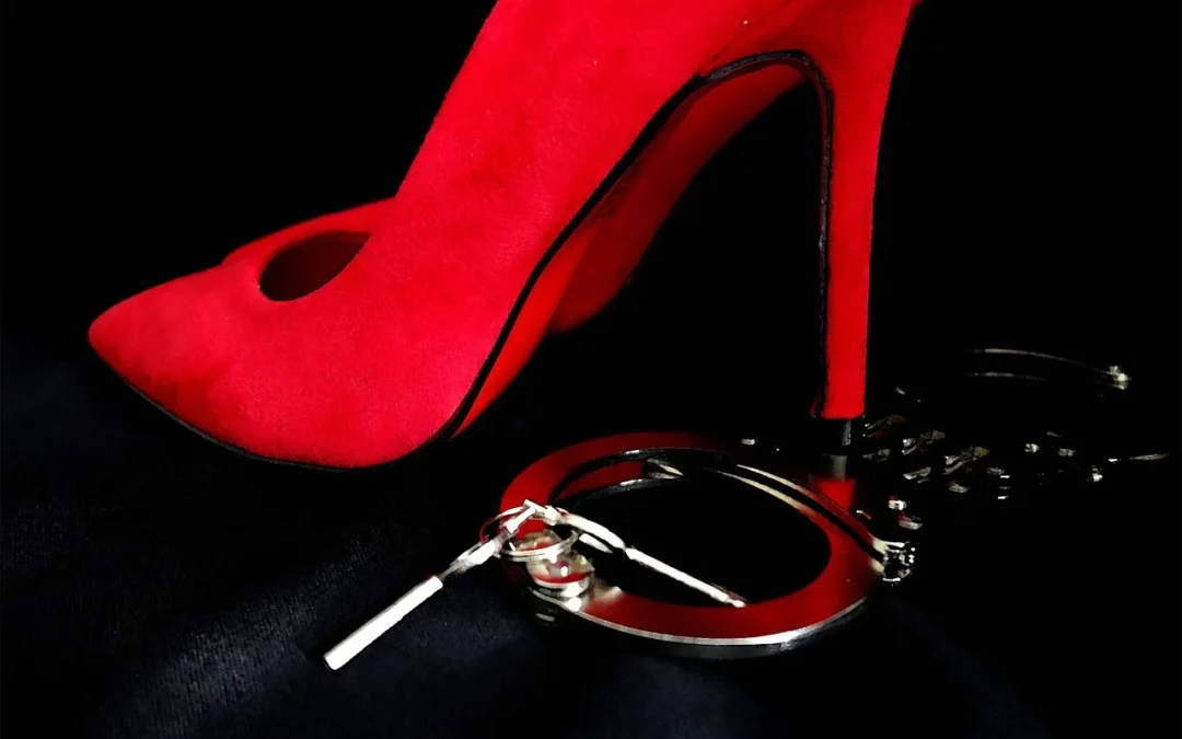 Chaussure à talon rouge et menottes sur fond noir.